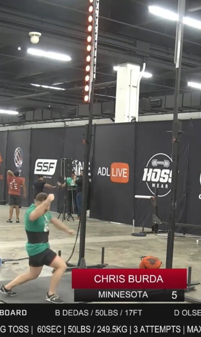 The scoring rig deployed at a live strongman bag-toss competition, light column visible on the pole behind the athlete
