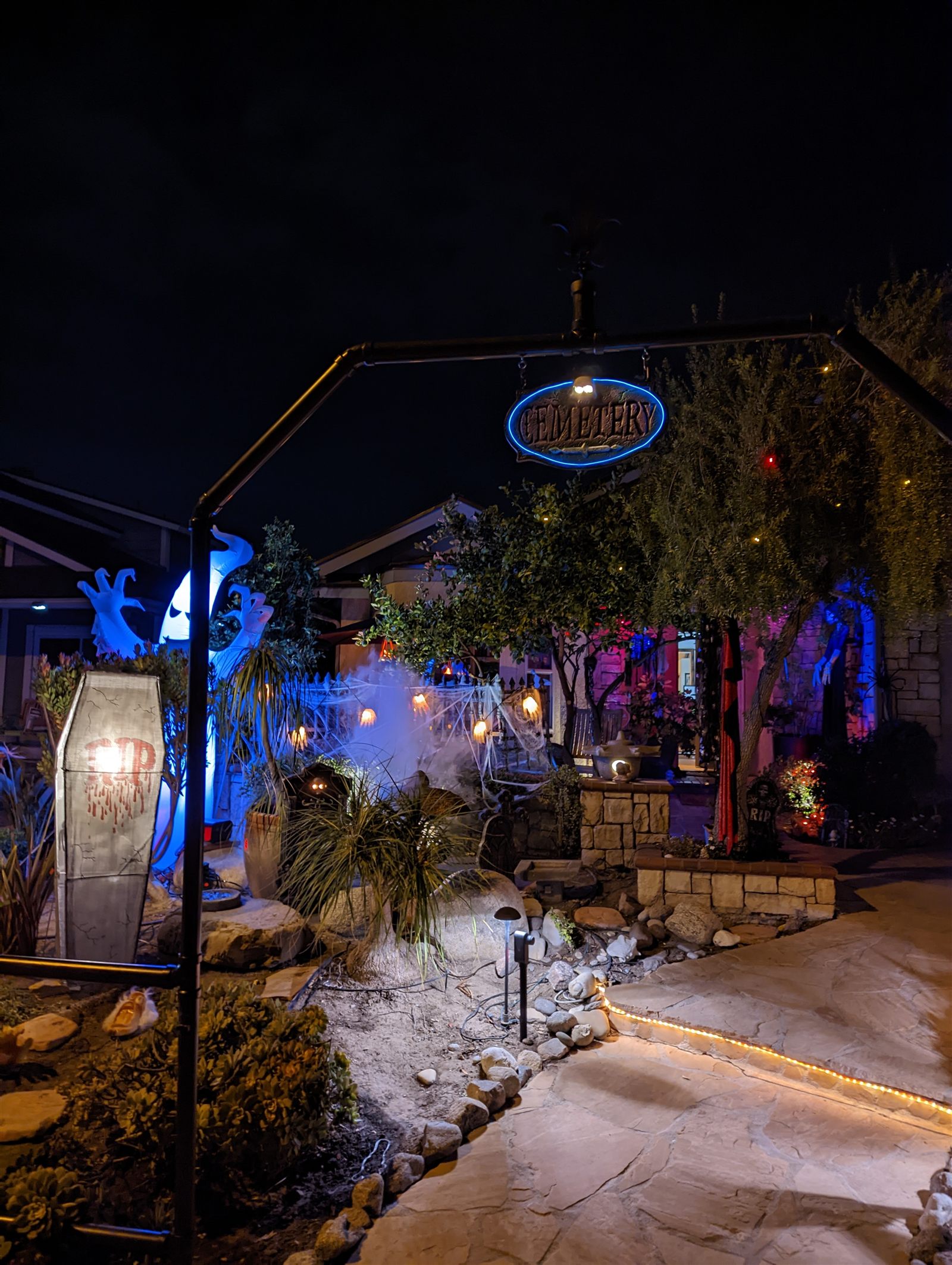 The front yard at night, decorated for Halloween with a lit "Cemetery" sign, fog, and a coffin prop